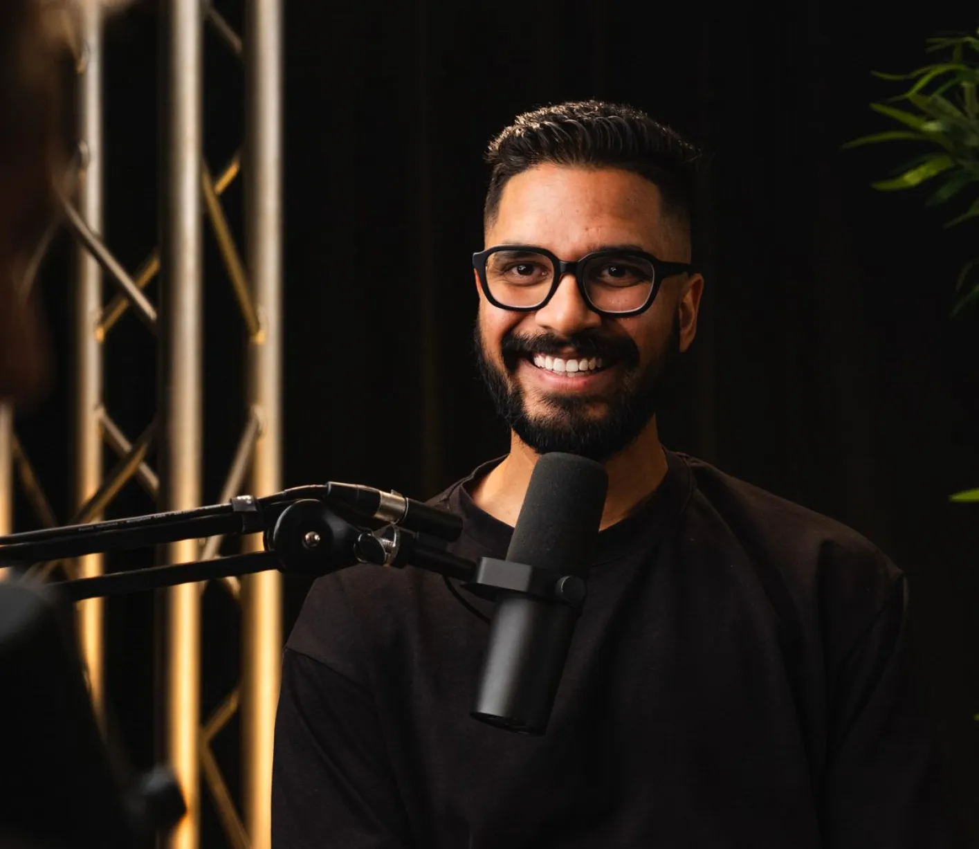 a man with glasses and a beard smiles while standing in front of a microphone