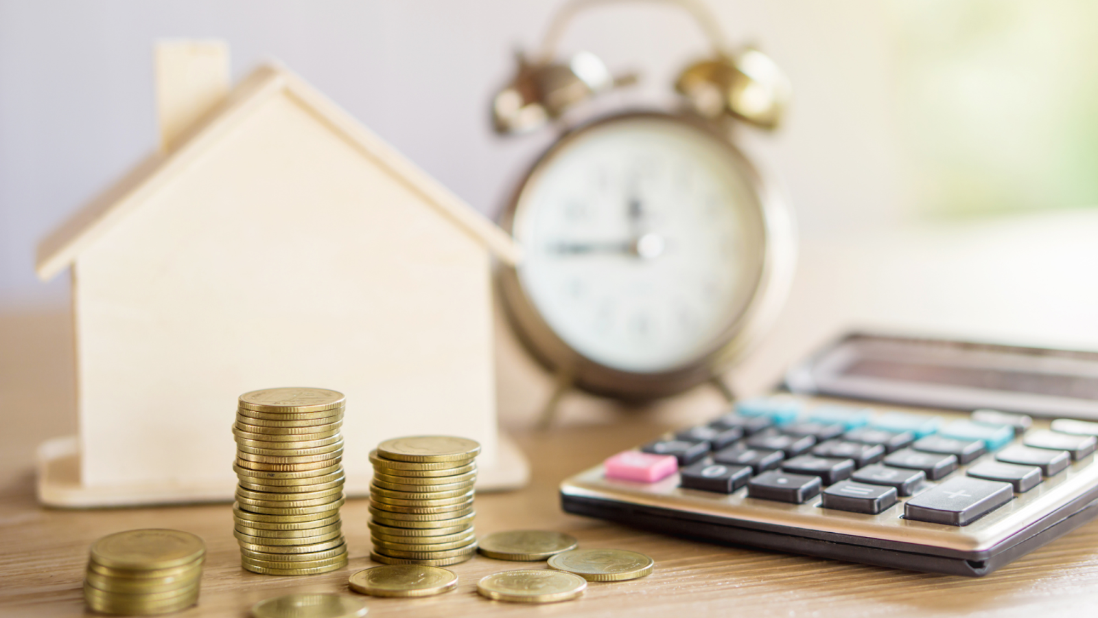 stacks of coins with a wooden house model, an alarm clock, and a calculator