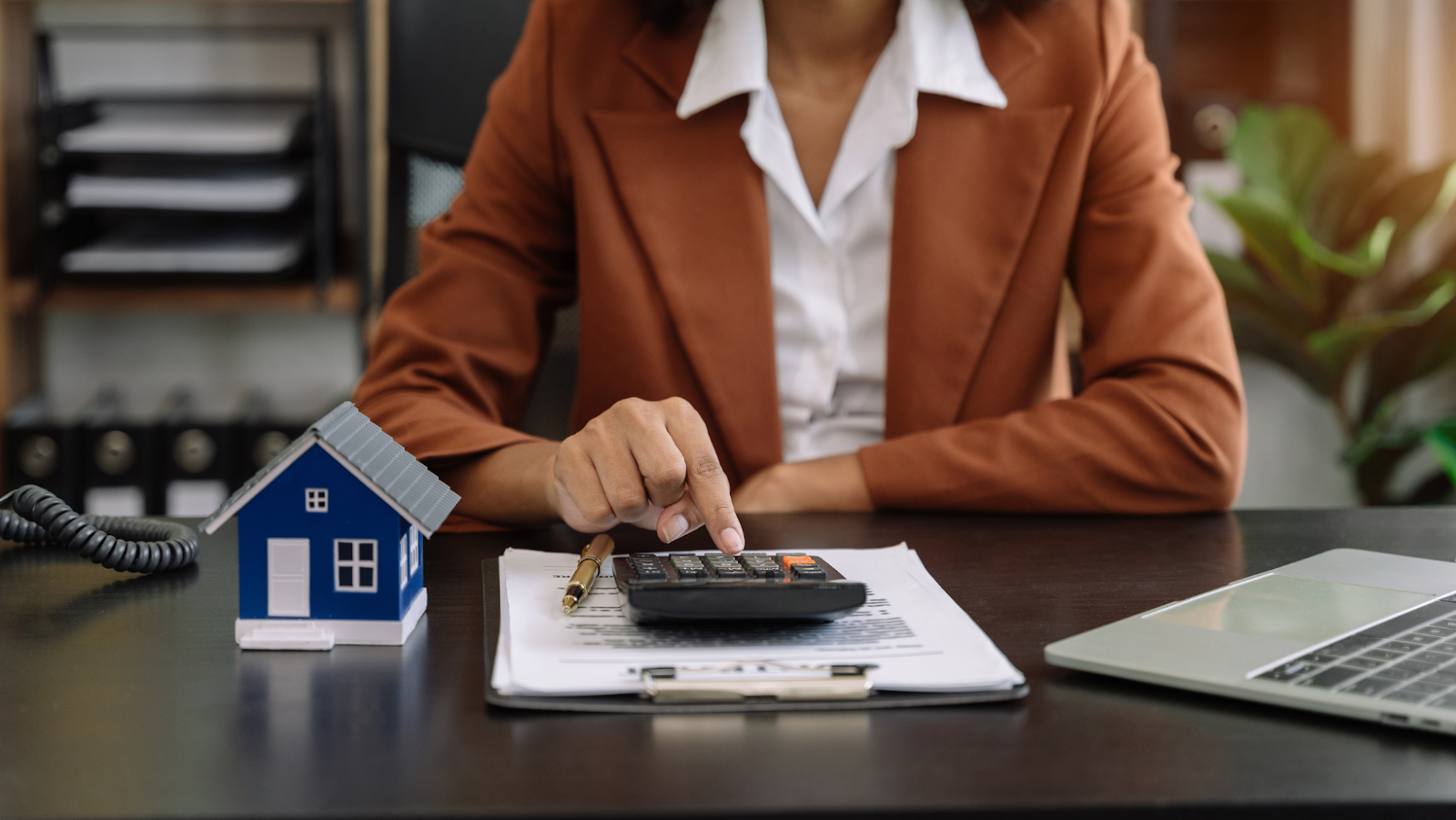 Businesswoman using a calculator with a small model house symbolising of a real estate investment
