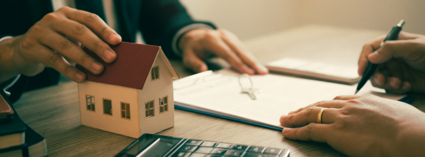 man wearing glasses looks at a house model in a hand, with real estate symbols