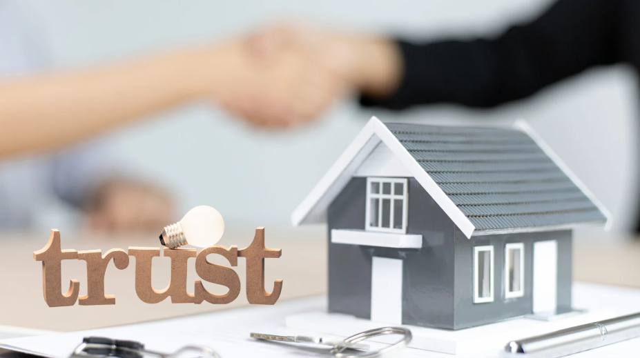 house model on a table with keys, documents, and a 'trust' sign, symbolizing a real estate agreement