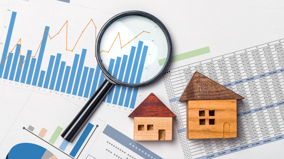 A magnifying glass over bar charts and financial data, with two wooden house models