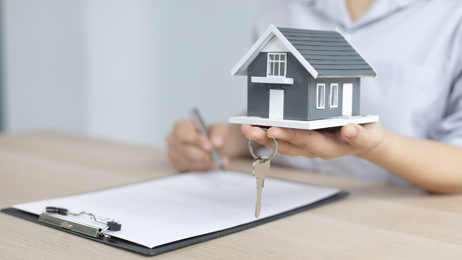 Person signing a contract while holding a model house with keys