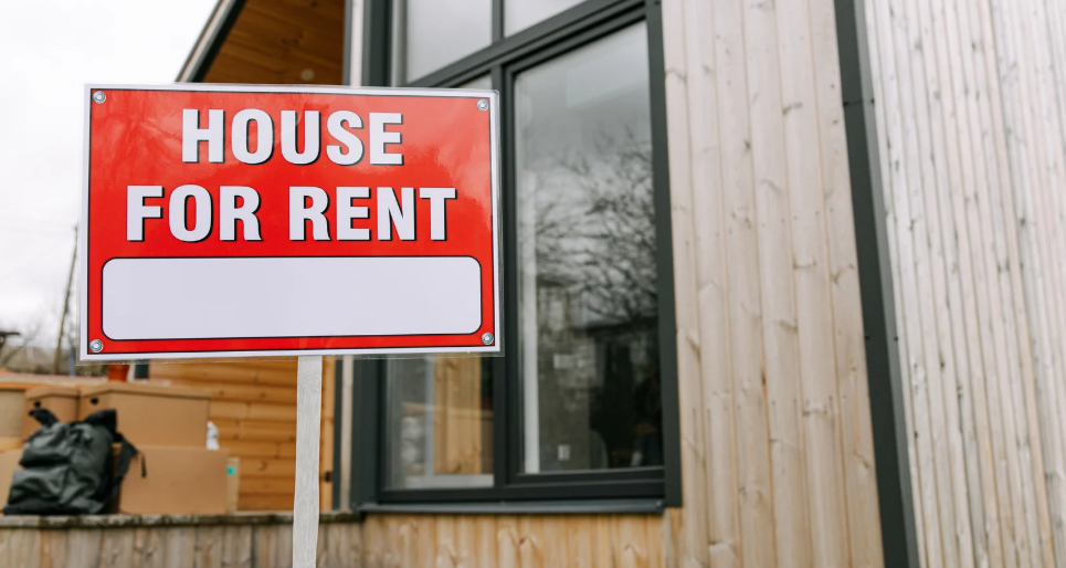 House For Rent sign positioned in front of a modern wooden-clad house