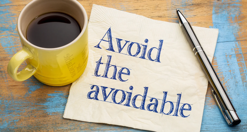 coffee cup beside a napkin with the message 'Avoid the avoidable' and a pen