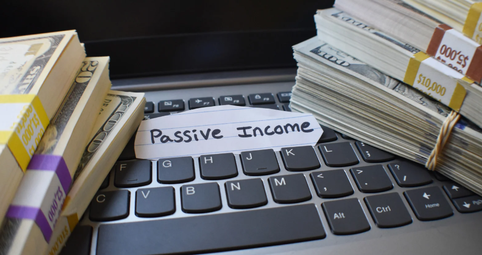 Stacks of U.S. dollar bills placed on a laptop keyboard with a label reading 'Passive Income' in the center.