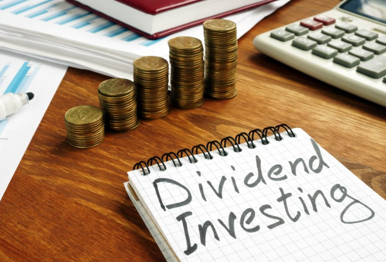Notebook with 'Dividend Investing' written on it, next to stacked coins, a calculator, and financial papers