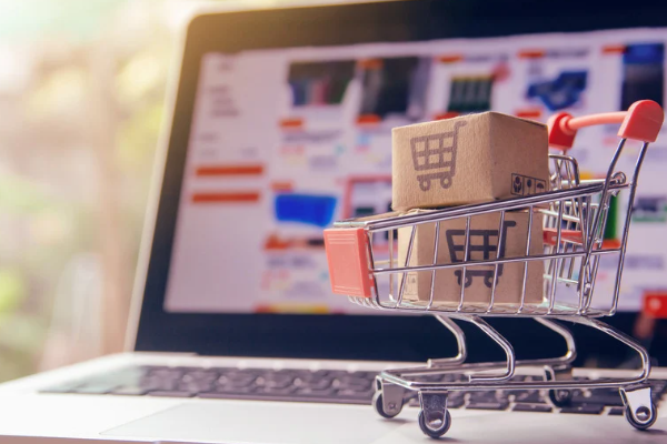 Mini shopping cart with cardboard boxes in front of a laptop screen displaying an online store.