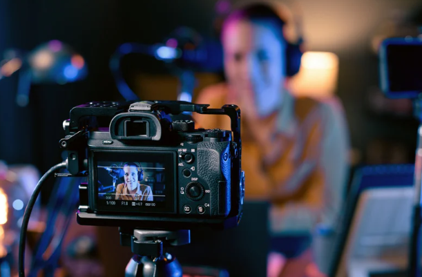 Camera recording a person wearing headphones in a dimly lit studio.