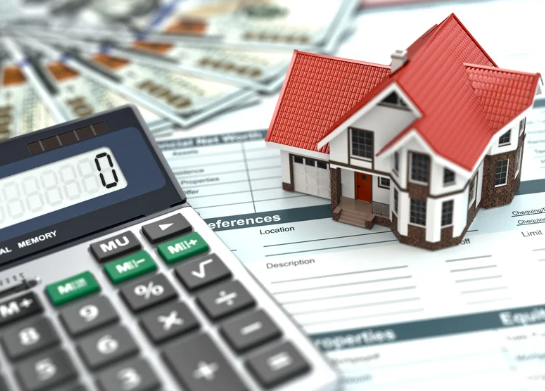 A miniature model of a house placed on top of financial documents, with a calculator showing zero and several US dollar bills spread out in the background.