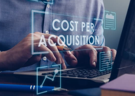 A person typing on a laptop with "COST PER ACQUISITION" displayed digitally in front of them, suggesting a focus on marketing metrics.