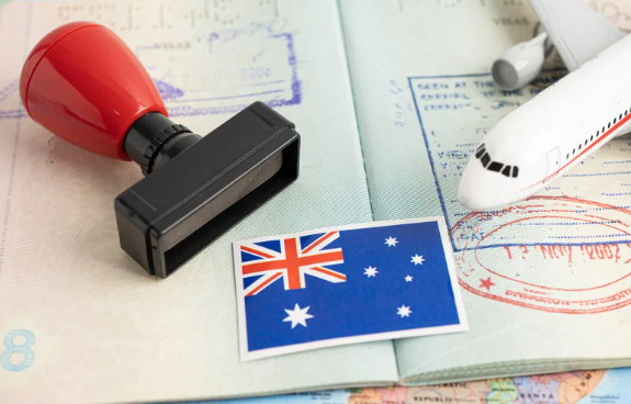 A rubber stamp, Australian flag postcard, and a miniature airplane on a passport backdrop, symbolizing travel to Australia.