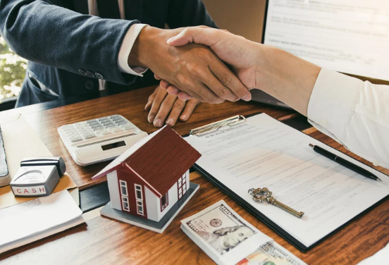 Real estate deal closing with handshake, contract, model house, cash, and keys on desk