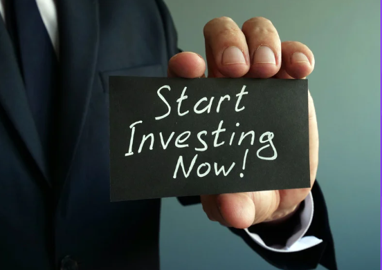 Close-up of a businessperson holding a black card with the handwritten message 'Start Investing Now!' promoting financial action