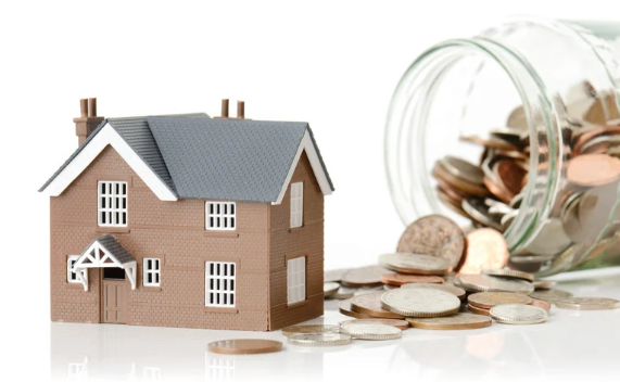 Miniature house beside a tipped-over bottle spilling coins