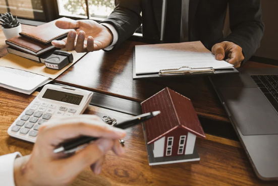 Two people discussing property investment, showing house model, contract, calculator, and laptop on desk