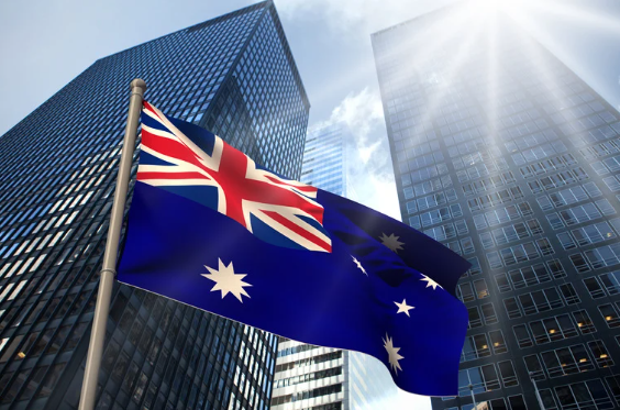 Australian flag waving in front of modern city skyscrapers under bright sunlight, symbolising economic growth and business opportunities in Australia.