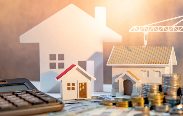 Real estate investment concept with model houses, construction crane, stacked coins, and calculator representing property growth and financing.