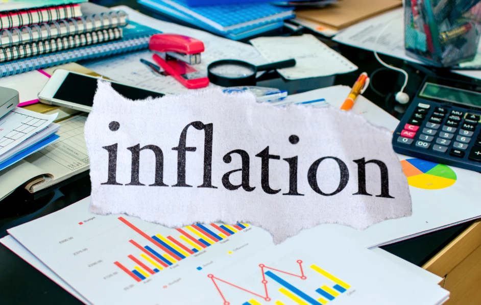 Inflation text with office desk items including calculators, property reports, graphs, notebook, stapler, pencil, magnifying glass, and smartphone symbolising financial analysis and rising costs.