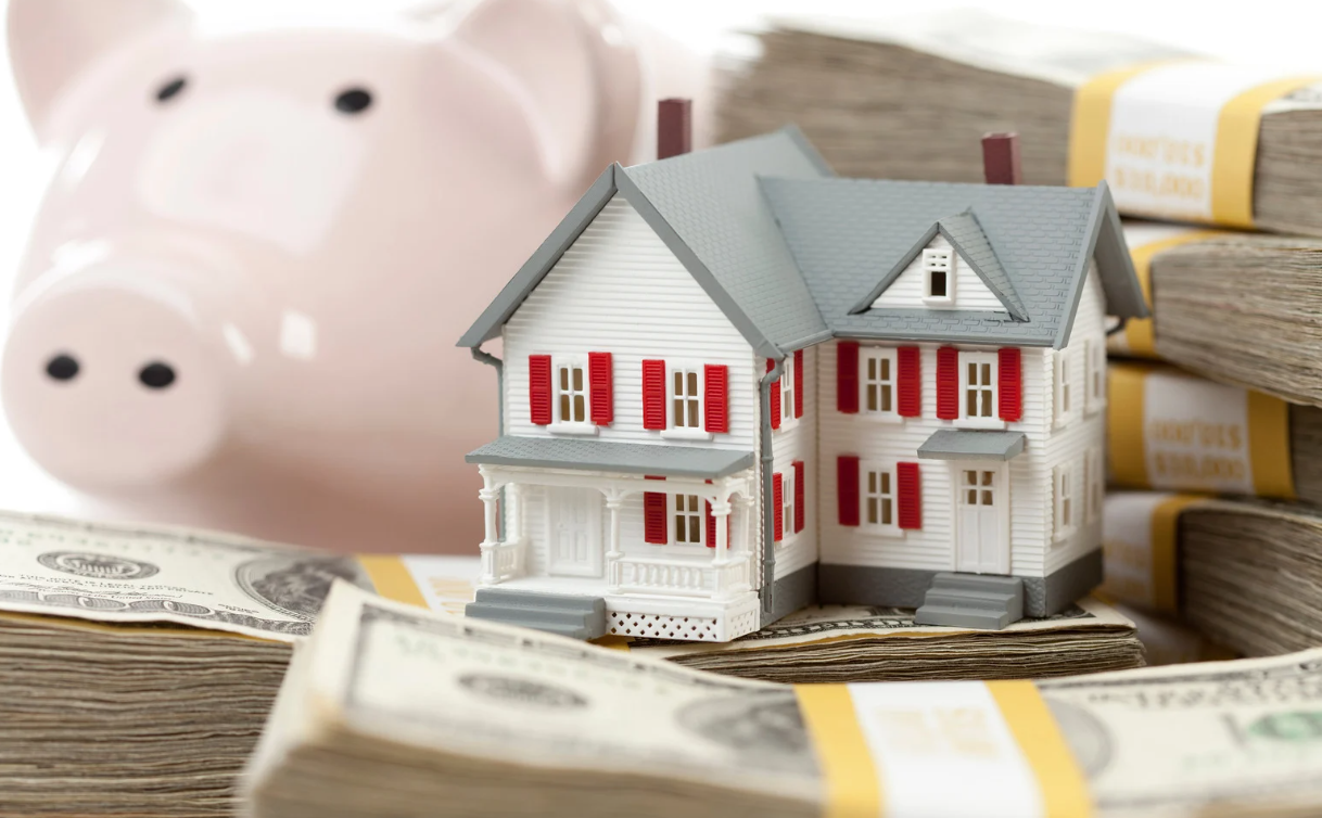 Piggy bank, miniature house, and stack of cash symbolizing property savings and investment.