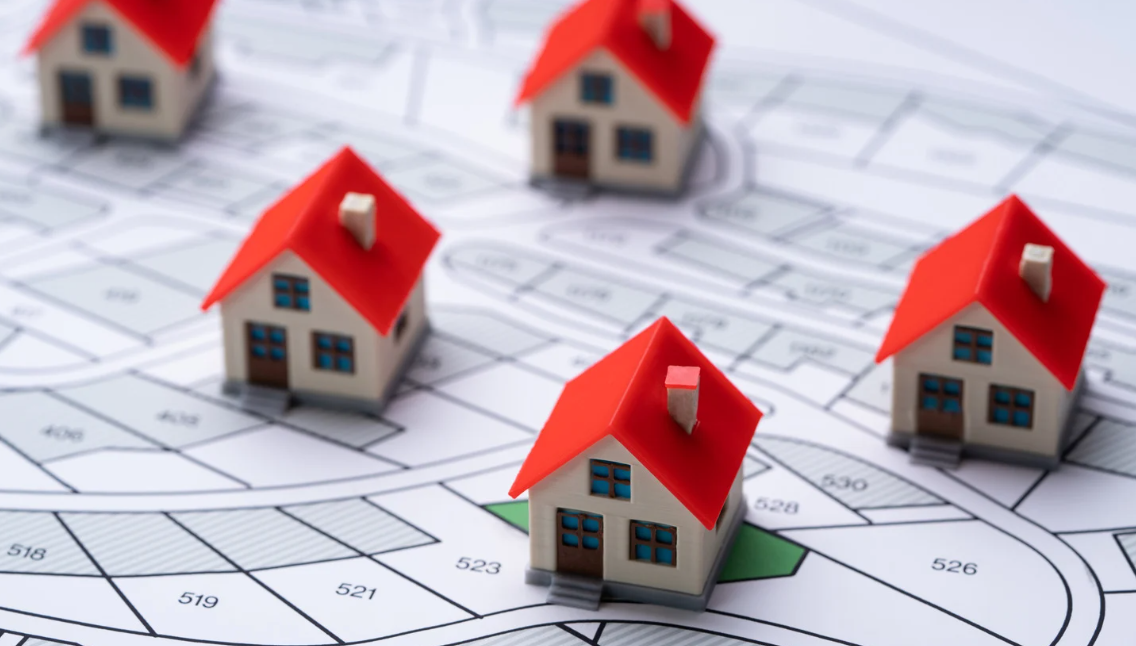 Miniature model houses with red roofs placed on a subdivision map, symbolising property investment, real estate planning, and land development.
