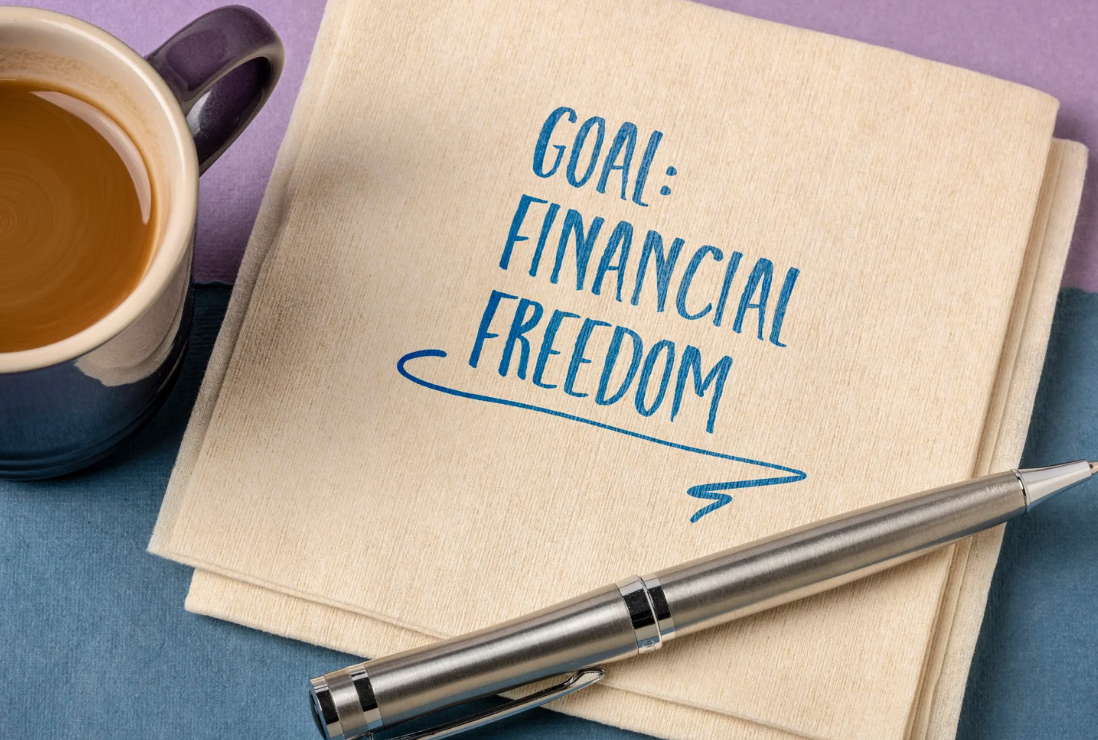 Coffee cup, tissue paper with a text that says “Goal: Financial Freedom” and a ballpen above it.