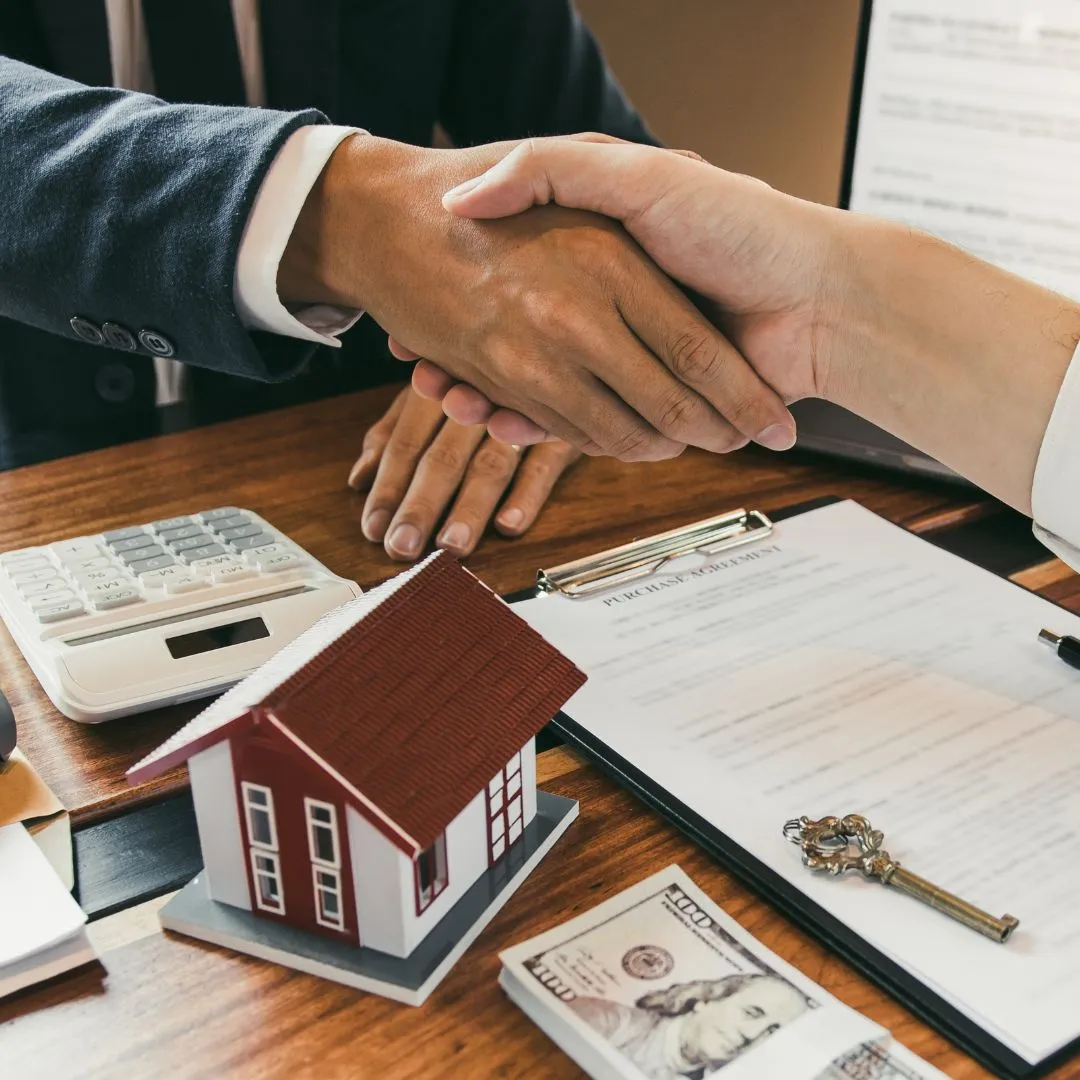 A couple of people shaking hands over a desk.