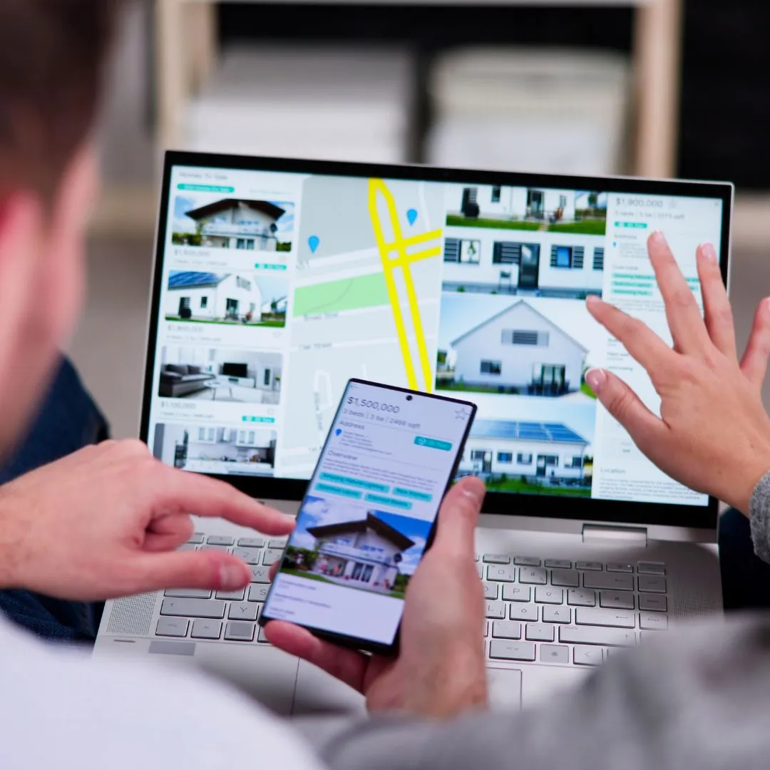 Two people looking at a laptop and a cell phone.