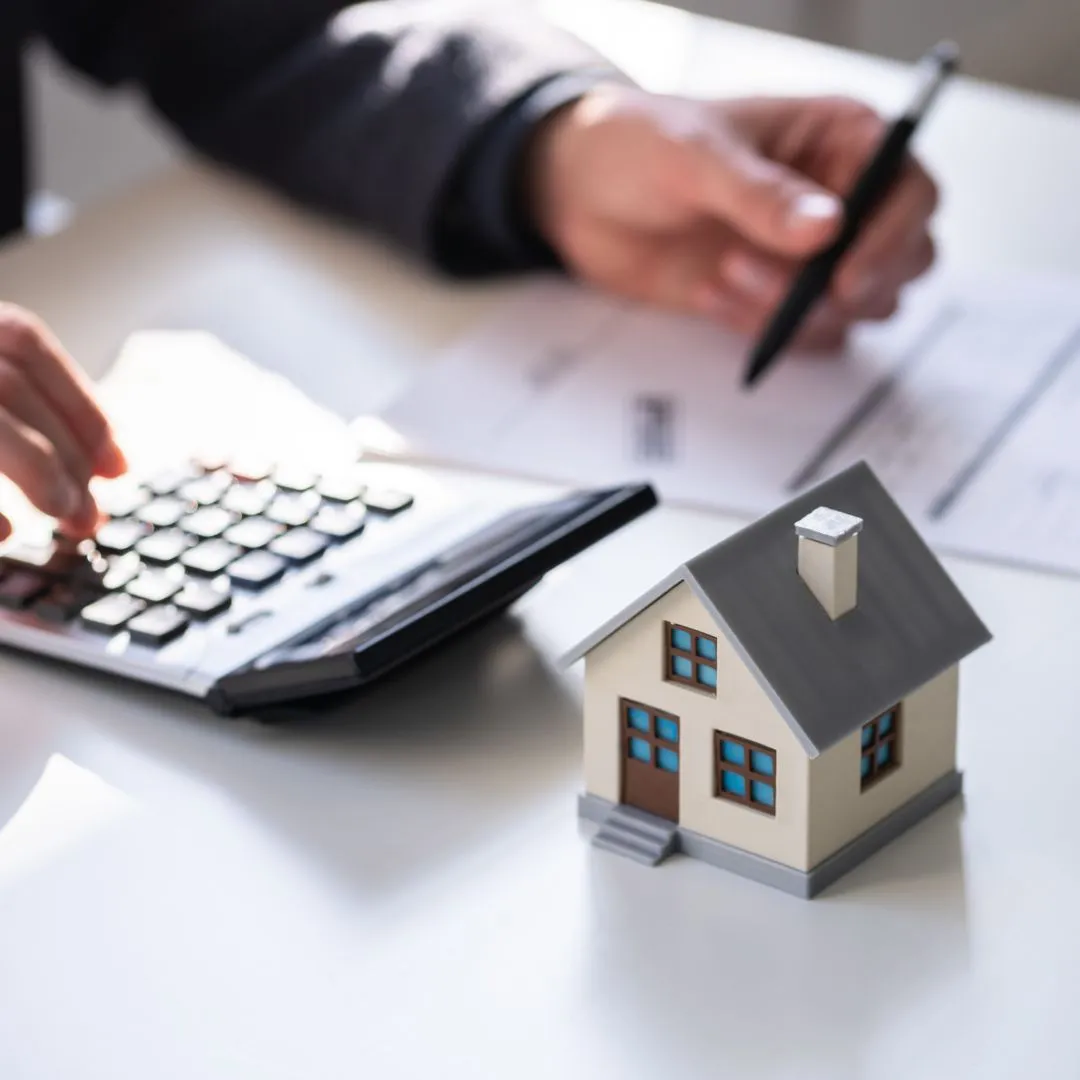 A person using a calculator next to a model house.