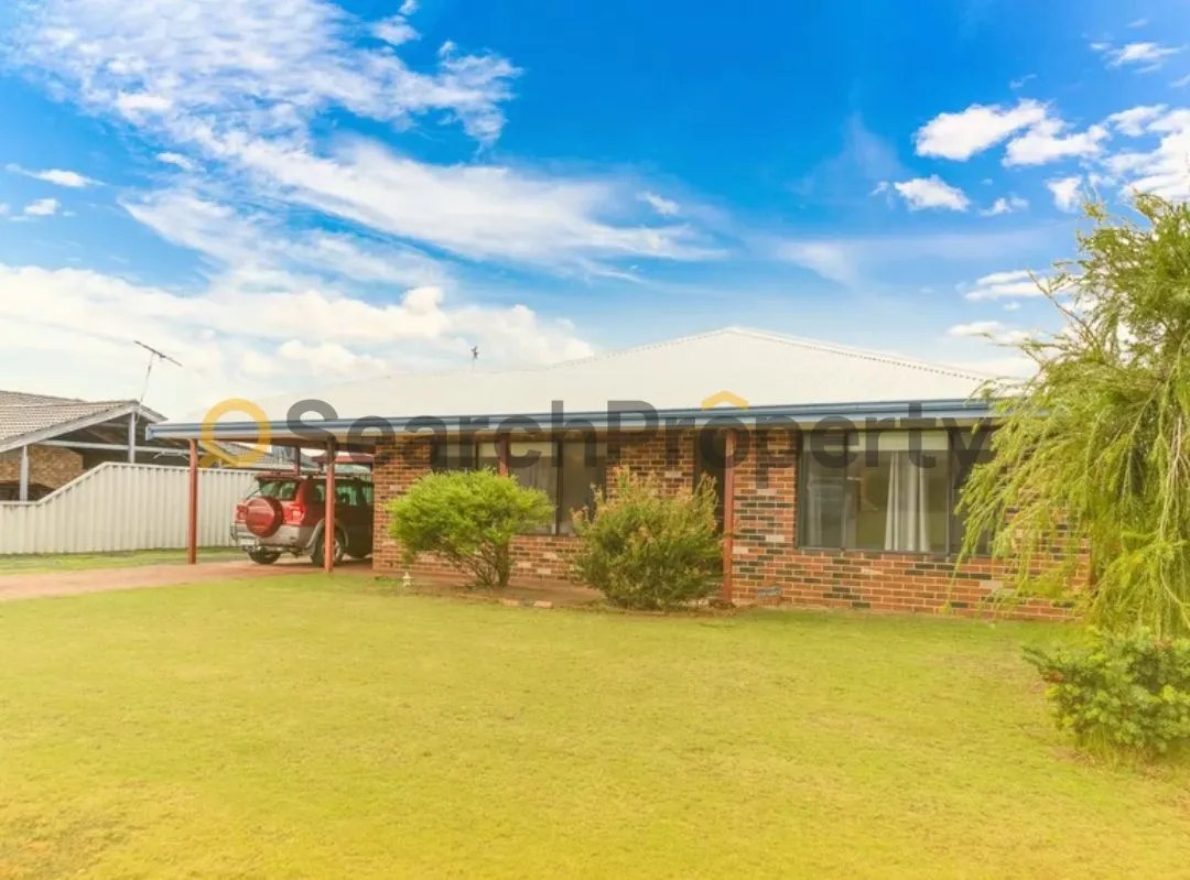 Single-storey brick home with a tin roof and front carport, featuring a well-kept lawn and driveway — a classic suburban investment property under a vibrant blue sky.