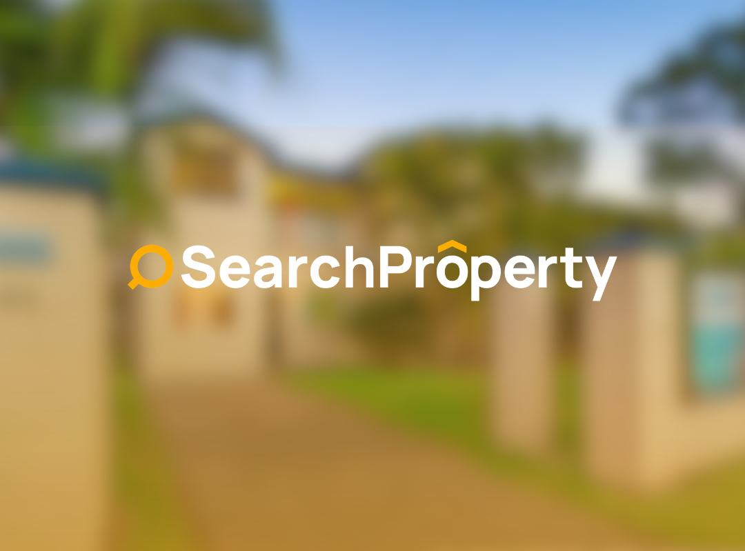 Single-storey brick home with a gated front entrance, paved driveway, landscaped lawn, and established tropical gardens in a quiet suburban Queensland neighbourhood under a clear blue sky.